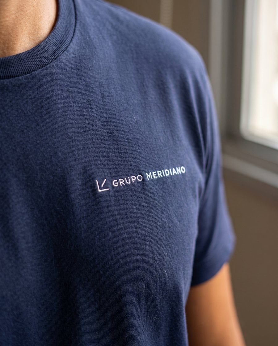 Detalhe da personalização: Logo “GRUPO MERIDIANO” bordado no peito.
