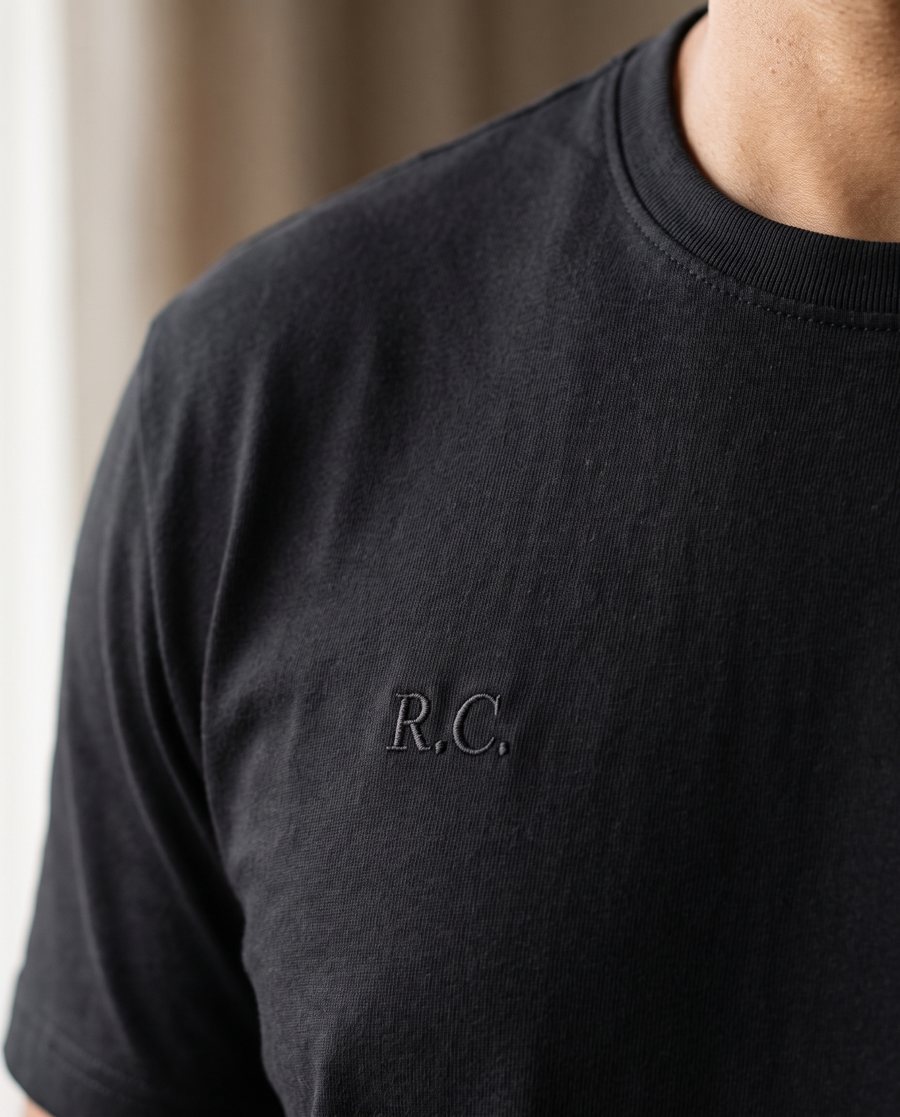 Camiseta preta com as iniciais R.C. bordadas tom sobre tom no peito