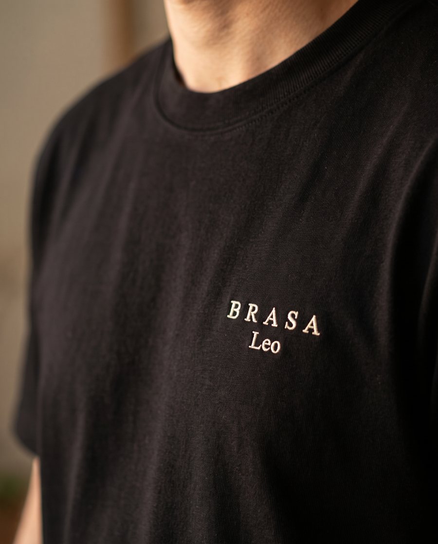 Detalhe de camiseta preta com o logo Brasa e o nome Leo bordados no peito